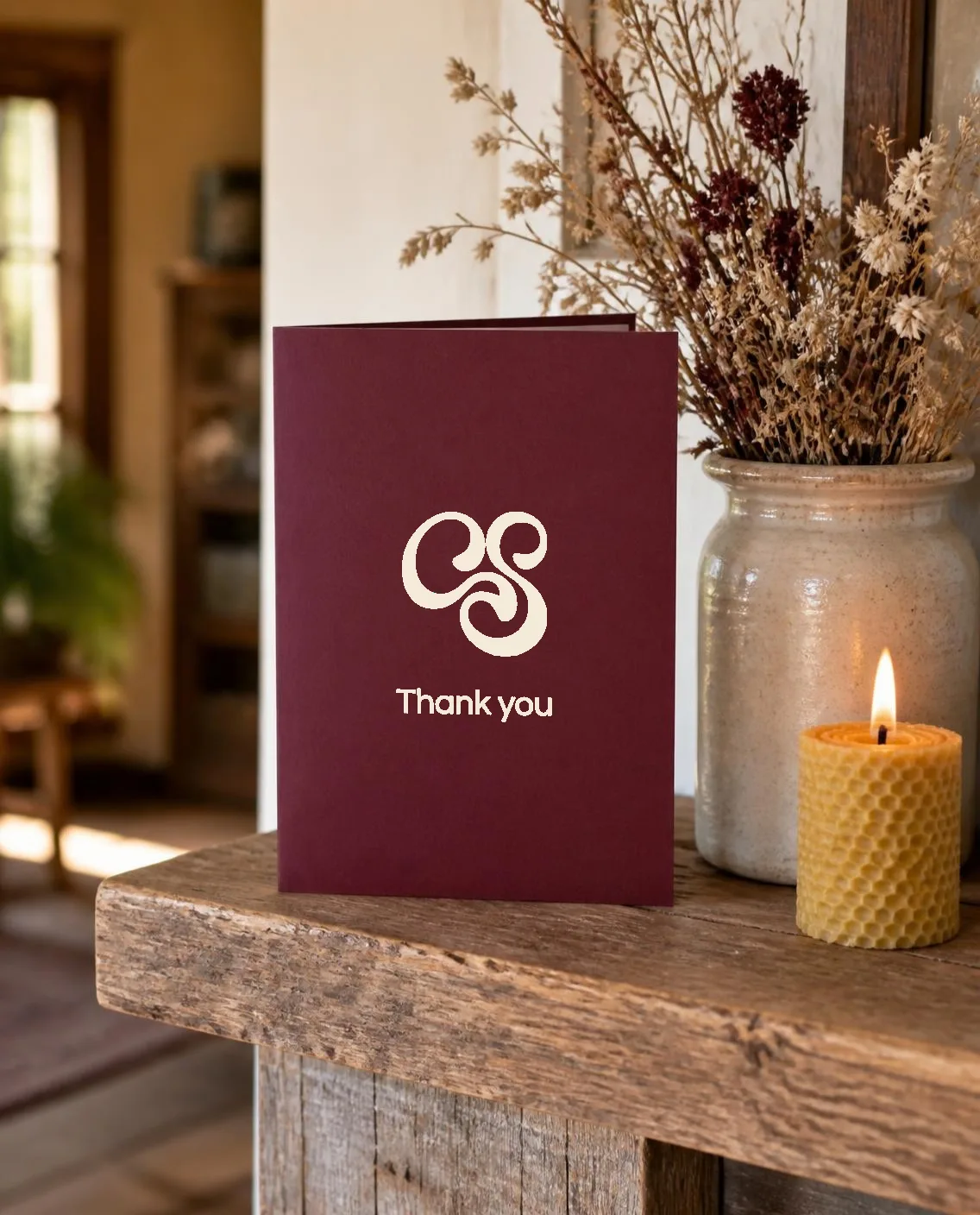 A merlot thank-you card with the off-white Curio monogram on a wooden mantel